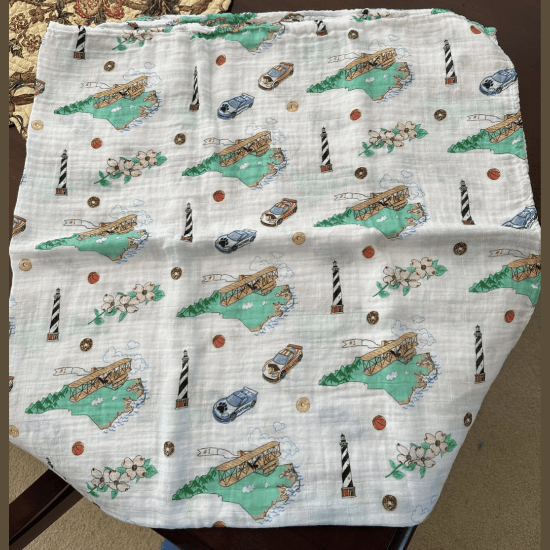North Carolina-themed baby gift set with muslin swaddle blanket, burp cloth, and bib in soft pastel colors.