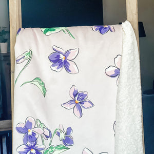 Soft, plush throw blanket in shades of violet and lavender, draped over a cozy, inviting surface.
