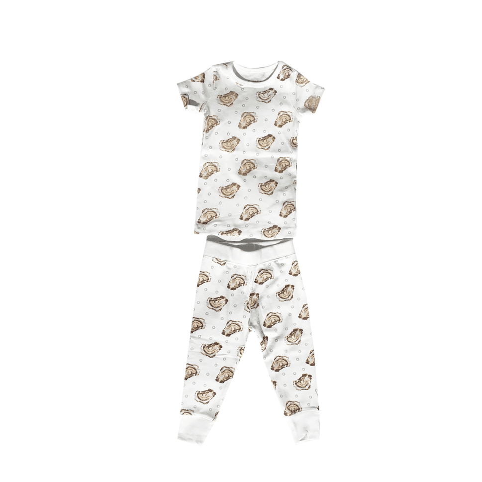 Toddler wearing "Aw Shucks" oyster-themed pajamas, smiling and holding a toy oyster, on a white background.