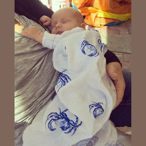 White muslin swaddle blanket with blue crab illustrations, featuring detailed claws and shells, on a white background.