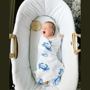 White muslin swaddle blanket with blue crab illustrations, folded neatly on a white background.