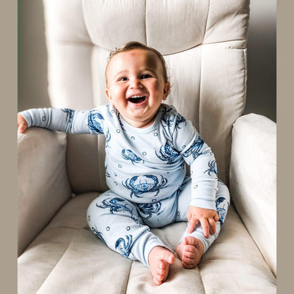 Toddler wearing blue pajamas with playful crab patterns, smiling and holding a stuffed animal in a cozy room.