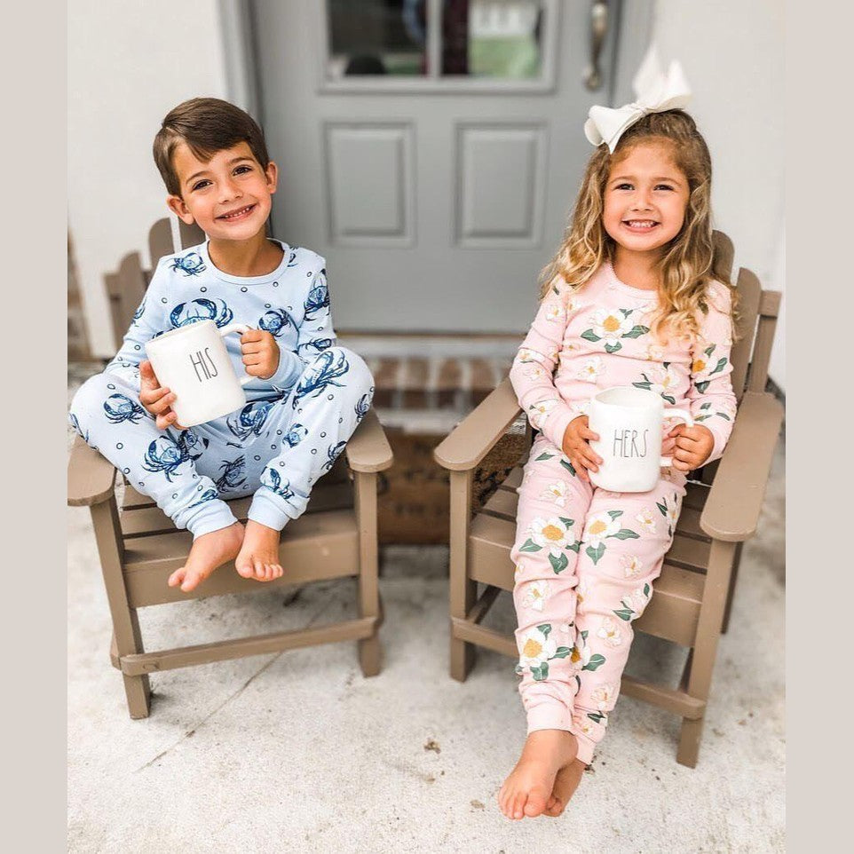 Toddler wearing blue pajamas with playful crab patterns, smiling and holding a stuffed animal in a cozy room.