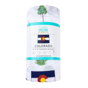 White muslin swaddle blanket with colorful Colorado-themed illustrations, including mountains, bears, and trees.
