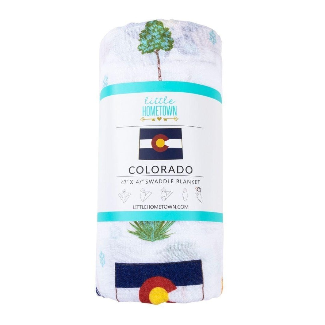 White muslin swaddle blanket with colorful Colorado-themed illustrations, including mountains, bears, and trees.