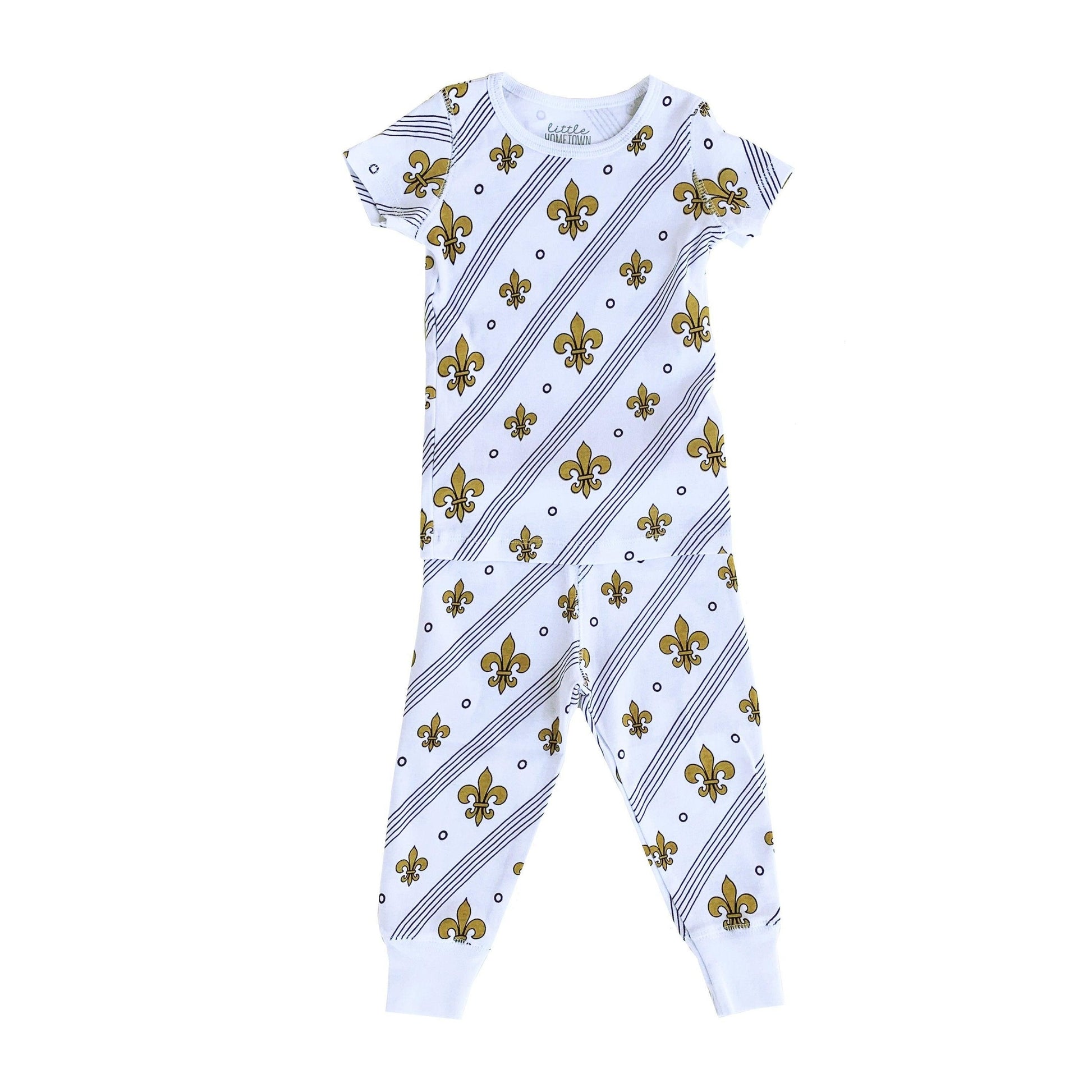 Toddler wearing white pajamas with blue fleur-de-lis pattern, smiling and holding a stuffed animal.