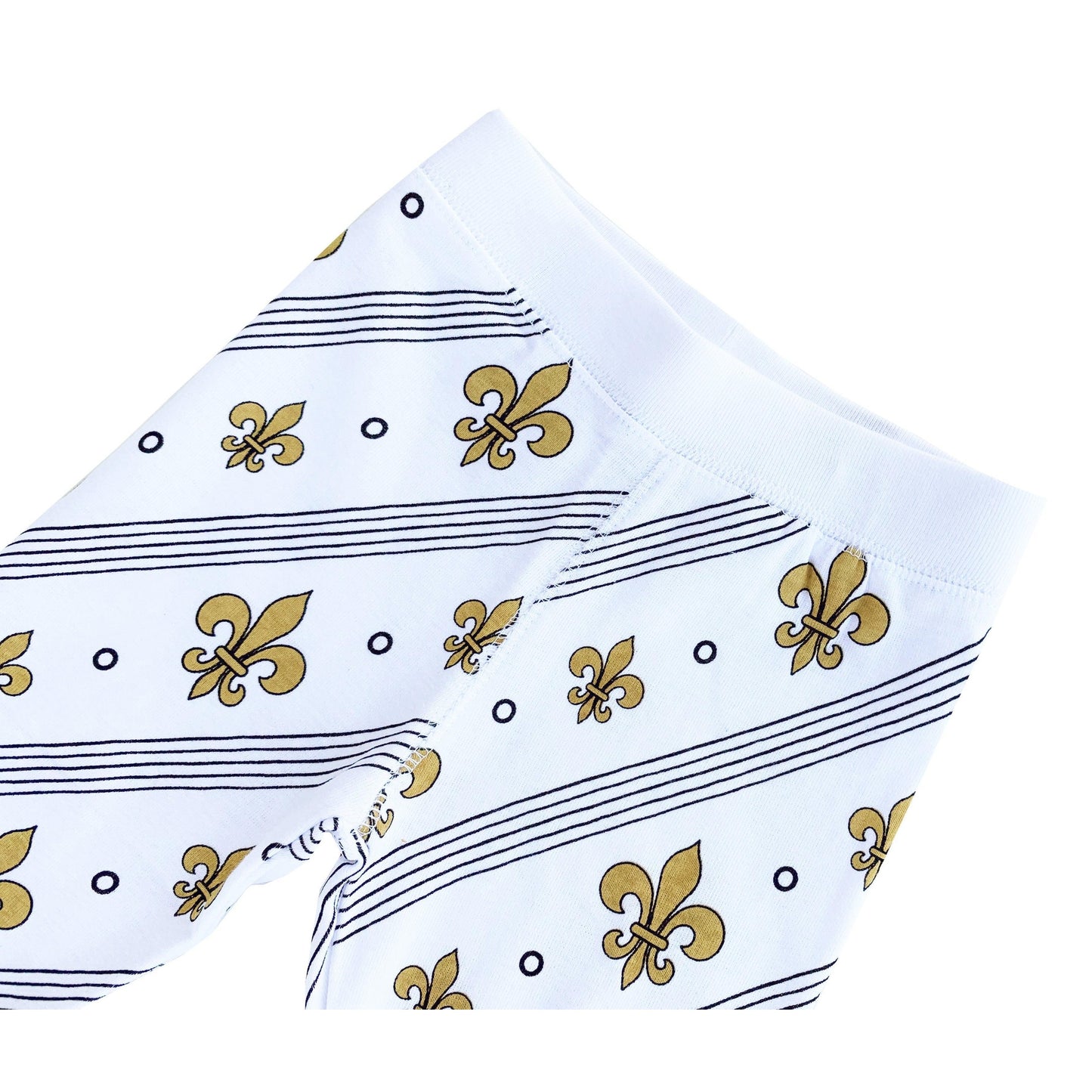 Toddler wearing white pajamas with blue fleur-de-lis pattern, smiling and sitting on a white bed.