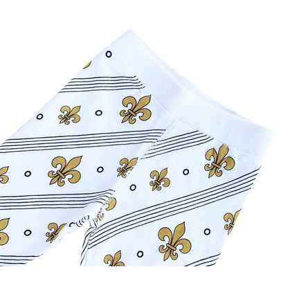 Toddler wearing white pajamas with blue fleur-de-lis pattern, smiling and sitting on a white bed.