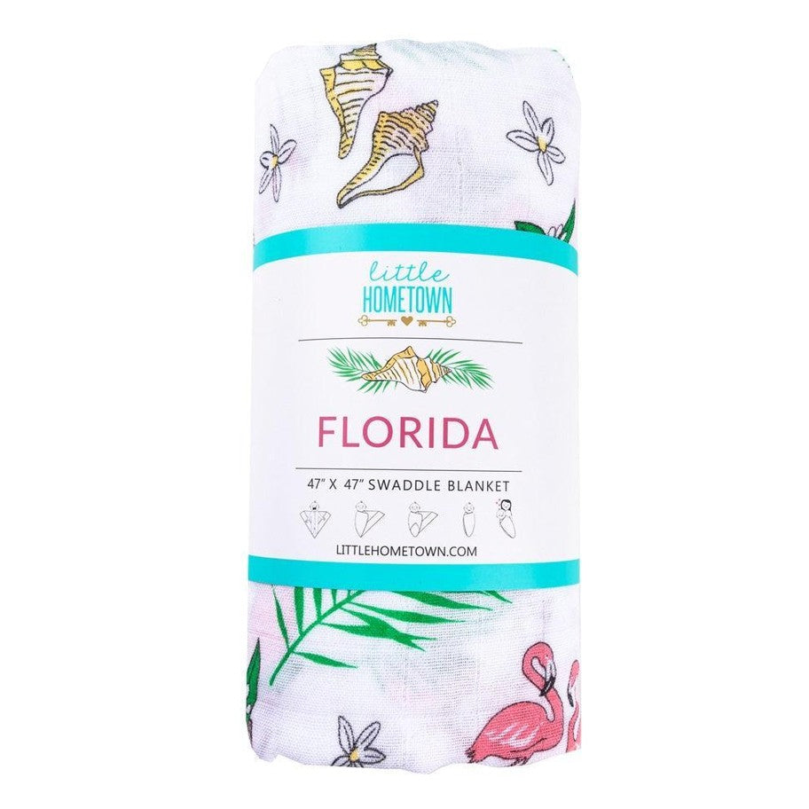 White muslin swaddle blanket with vibrant floral patterns, featuring pink hibiscus and green palm leaves.