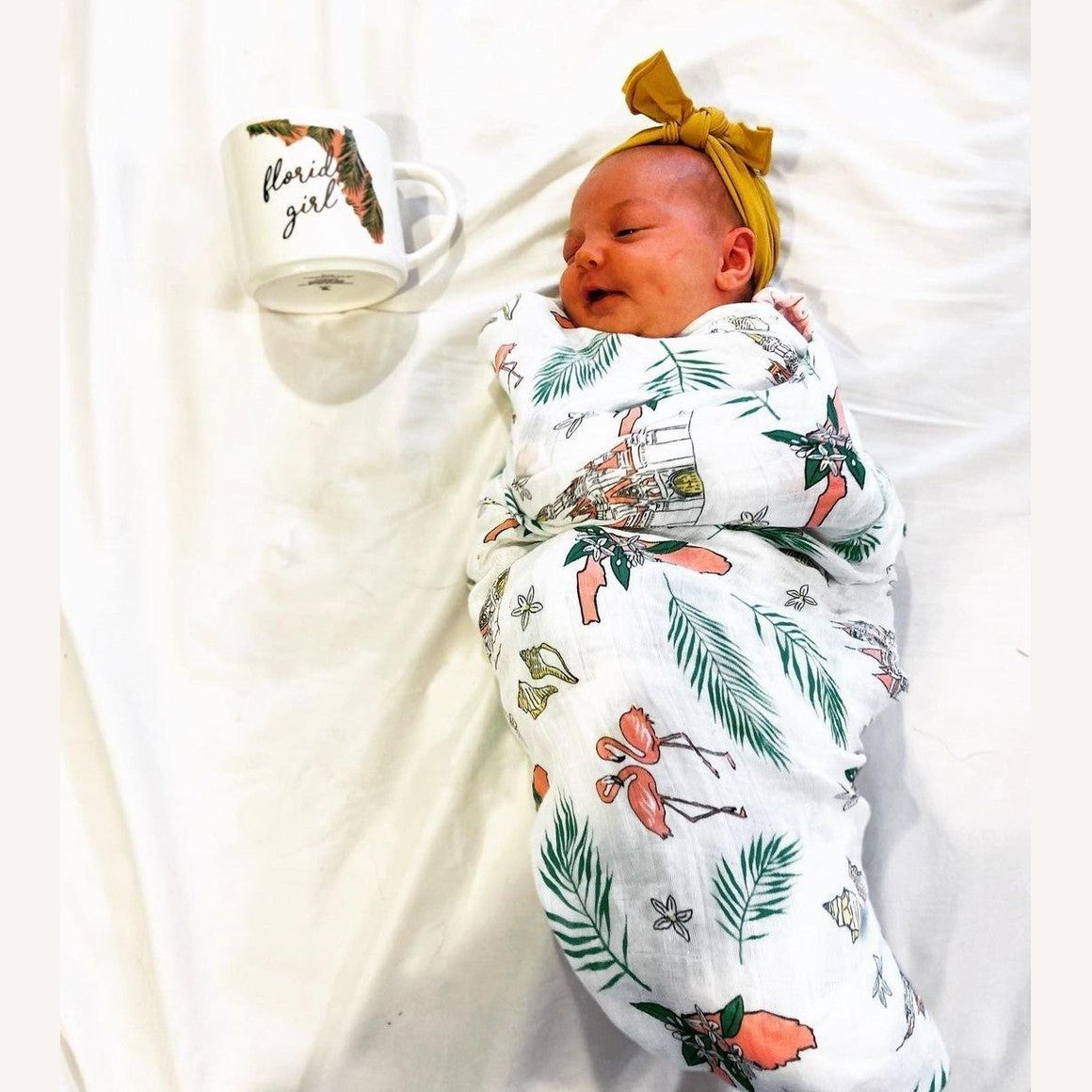 White muslin swaddle blanket with colorful floral print, featuring pink, yellow, and green flowers.