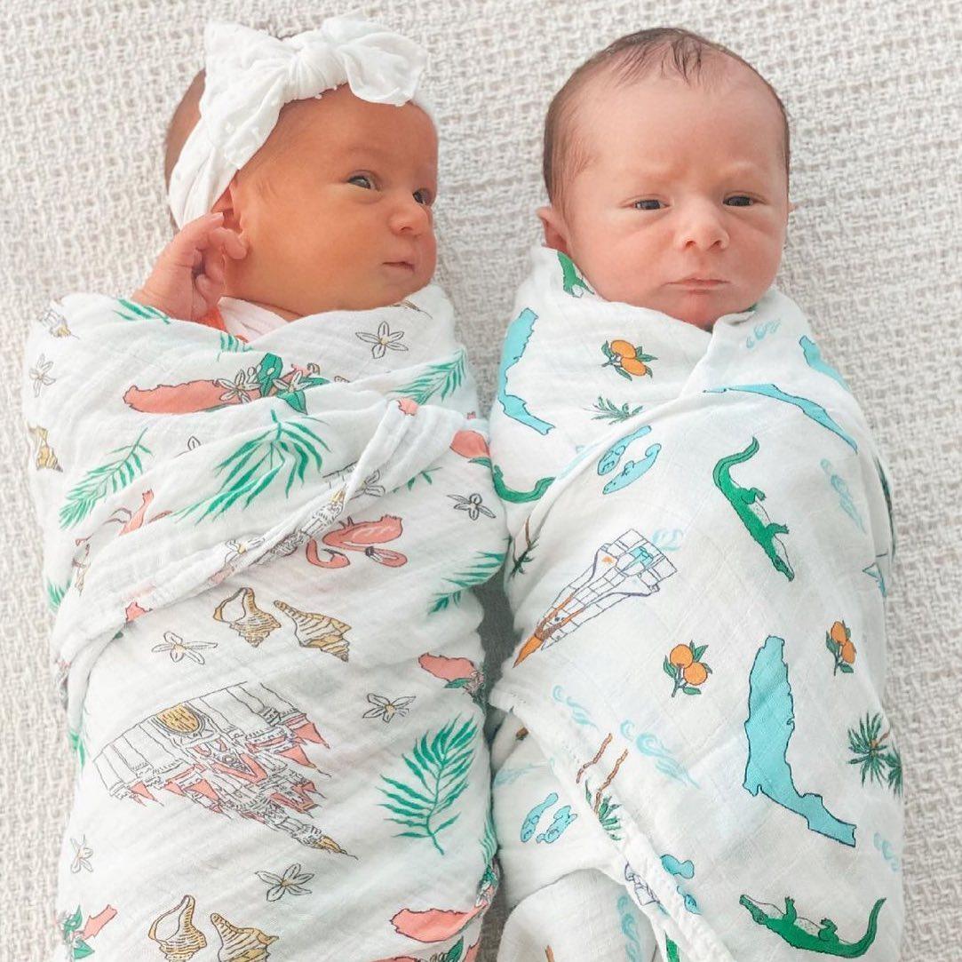 White muslin swaddle blanket with colorful floral print, featuring pink, yellow, and green flowers.