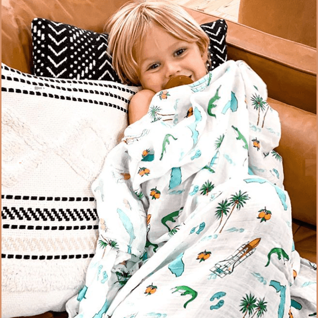 White muslin swaddle blanket with colorful Florida-themed illustrations, including oranges, flamingos, and palm trees.