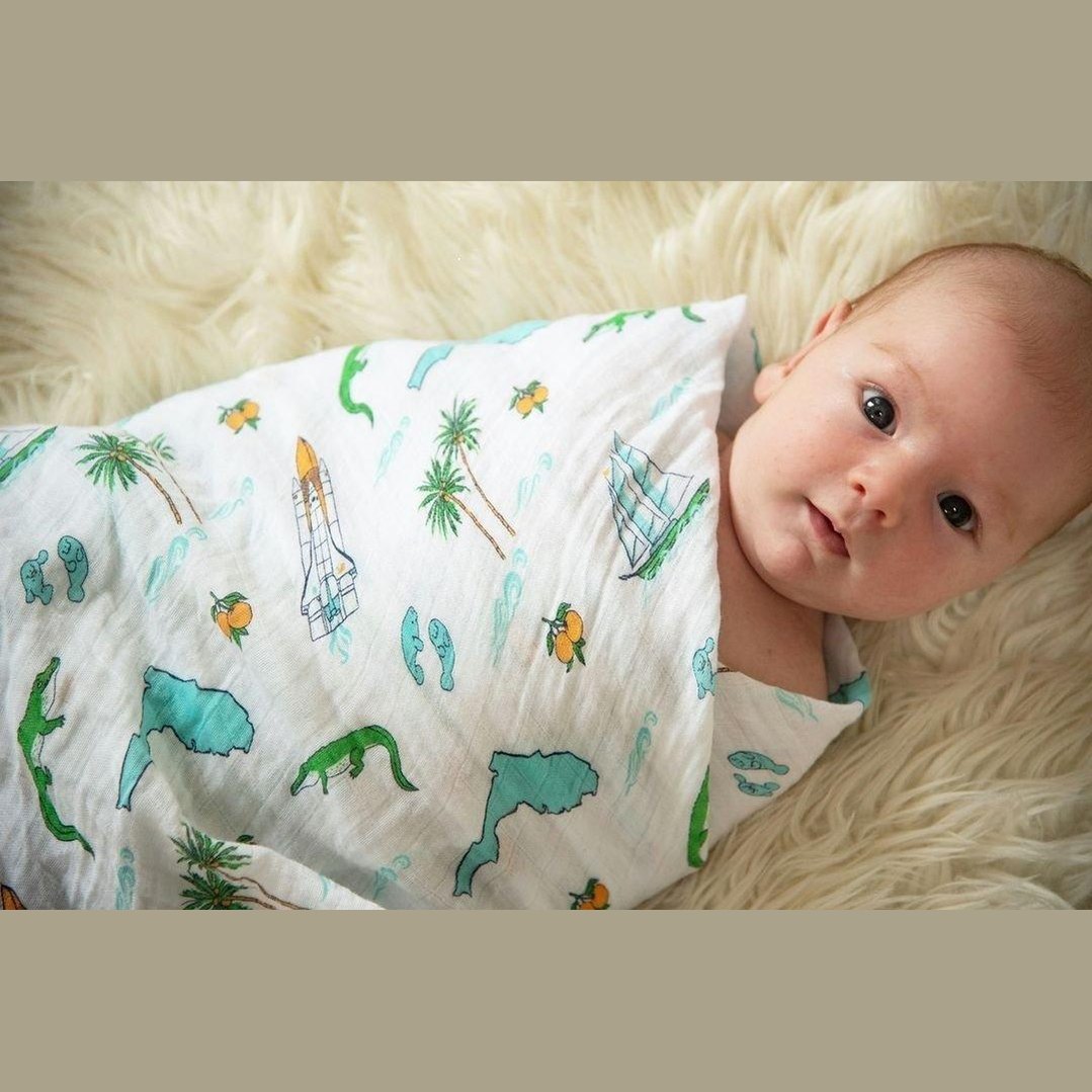 White muslin swaddle blanket with colorful Florida-themed illustrations, including oranges, flamingos, and palm trees.