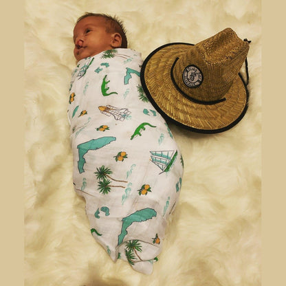 Florida-themed baby muslin swaddle blanket with colorful illustrations of palm trees, flamingos, and oranges.