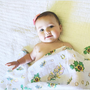 Floral-themed baby gift set with a muslin swaddle blanket and burp cloth/bib combo, featuring pink and green flowers.