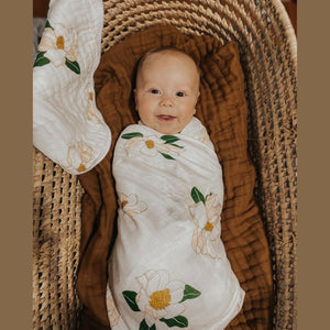 Southern Magnolia baby muslin swaddle blanket and burp cloth set with delicate floral design on a white background.