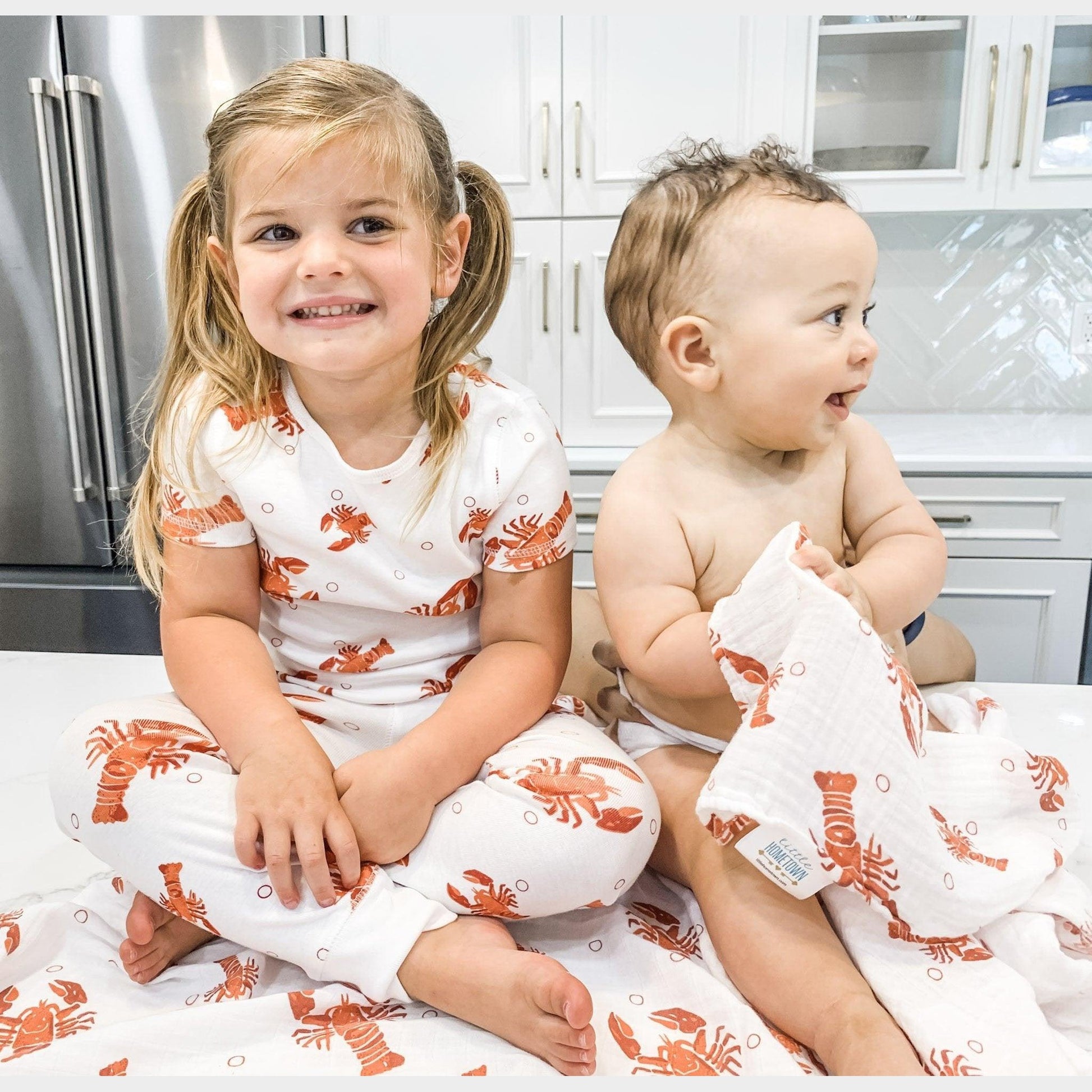 Toddler wearing white pajamas with red lobsters and blue crawfish, smiling and holding a toy lobster.