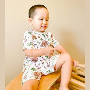 Toddler wearing colorful Jambalaya-themed pajamas with shrimp, sausage, and rice illustrations, smiling joyfully.