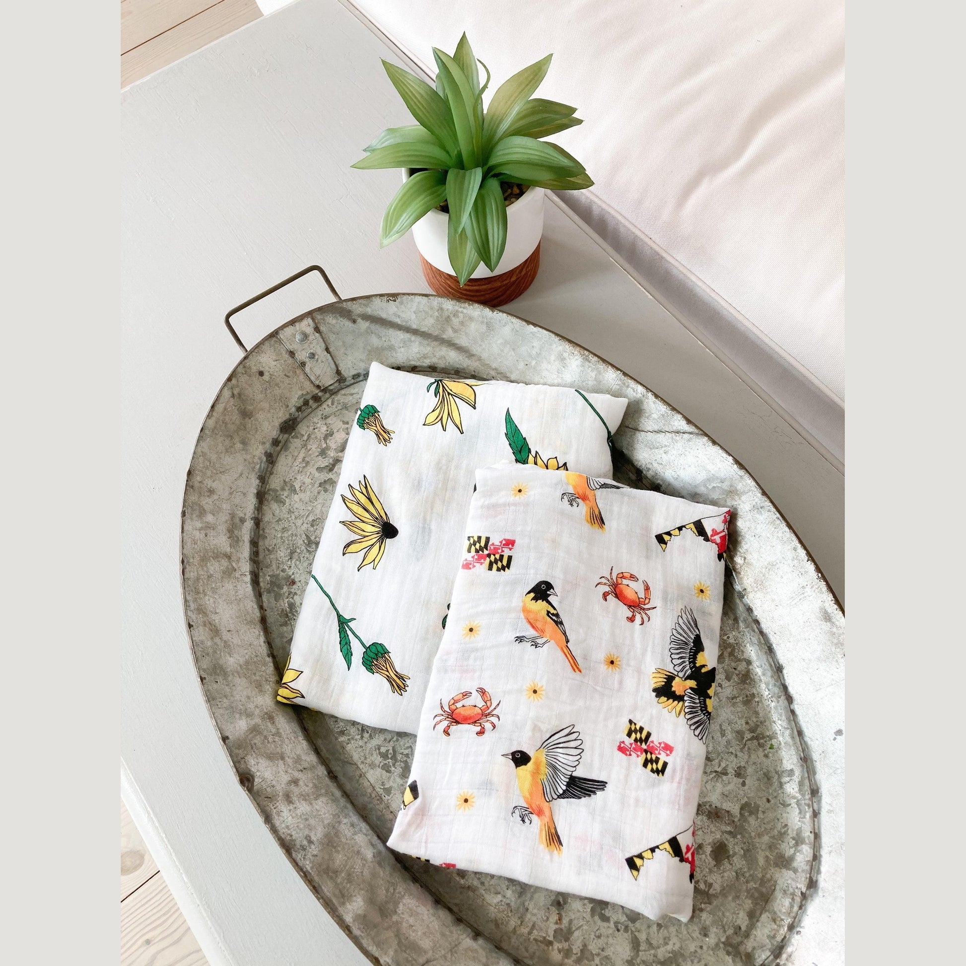 White muslin baby swaddle blanket with Maryland-themed illustrations, including crabs, flags, and lighthouses.