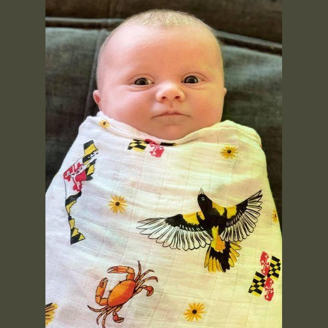 White muslin baby swaddle blanket with Maryland-themed illustrations, including crabs, lighthouses, and state symbols.