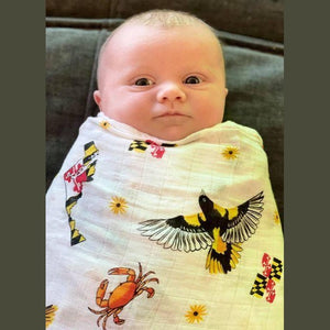 White muslin baby swaddle blanket with Maryland-themed illustrations, including crabs, lighthouses, and state symbols.