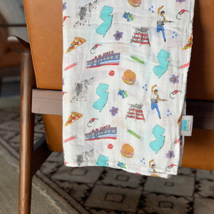 White muslin swaddle blanket with a colorful New Jersey map, featuring landmarks, animals, and state symbols.