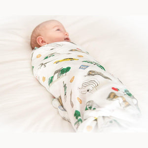 White muslin swaddle blanket featuring a colorful, whimsical map of New York City with landmarks and icons.