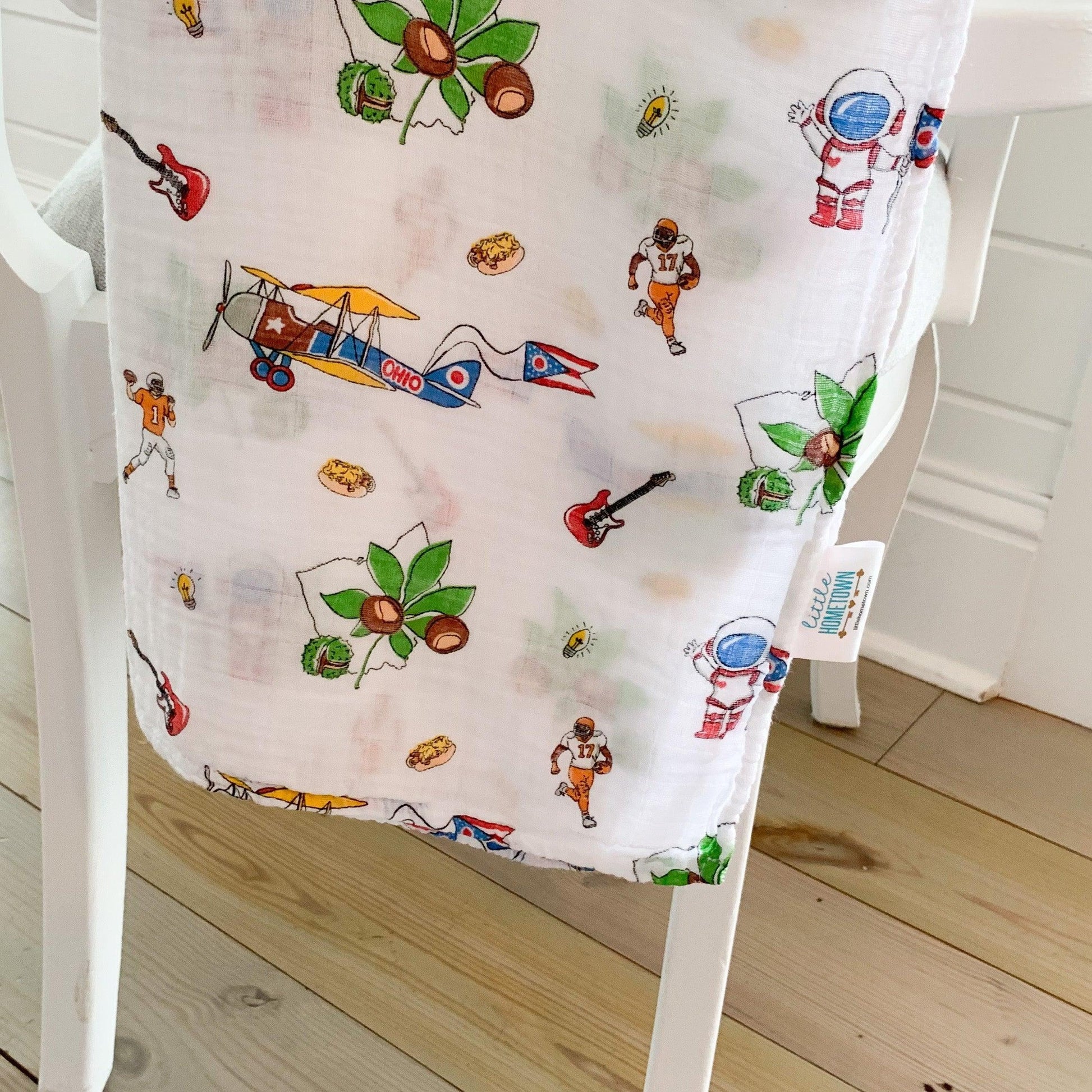 Ohio-themed baby muslin swaddle blanket with state icons and landmarks in soft pastel colors on a white background.
