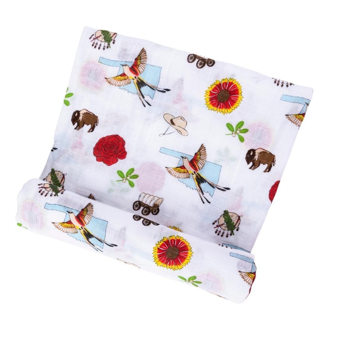 Oklahoma-themed baby swaddle blanket with state icons and landmarks in soft pastel colors on a white background.