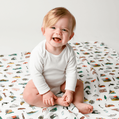 White muslin swaddle blanket with Seattle skyline, Space Needle, and Mount Rainier illustrations in soft pastel colors.