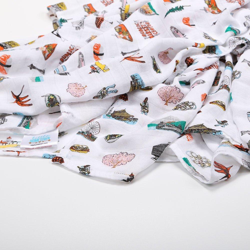 White muslin swaddle blanket with Seattle landmarks like the Space Needle and Pike Place Market, in soft pastel colors.