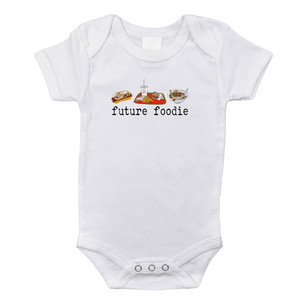 White onesie with "Seattle Foodie" text and icons of coffee, fish, and a Space Needle on a wooden background.