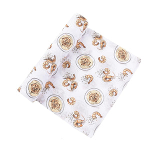 White muslin swaddle blanket with playful shrimp and grits illustrations, featuring vibrant orange and yellow hues.
