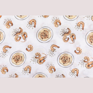 White muslin swaddle blanket with colorful shrimp and grits pattern, featuring bowls, shrimp, and corn.