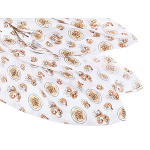 White muslin swaddle blanket with playful shrimp and grits illustrations, featuring vibrant orange and yellow hues.