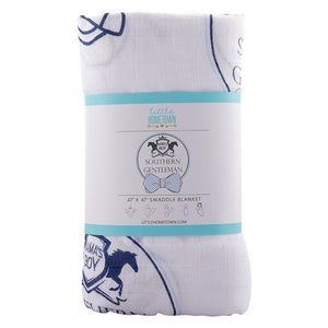 Baby boy swaddled in a white muslin blanket with blue bow ties and mustaches, lying on a soft surface.