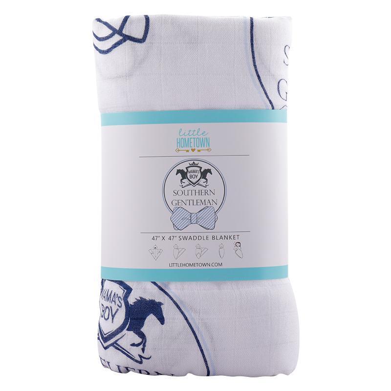 Baby boy swaddled in a white muslin blanket with blue bow ties and mustaches, lying on a soft surface.