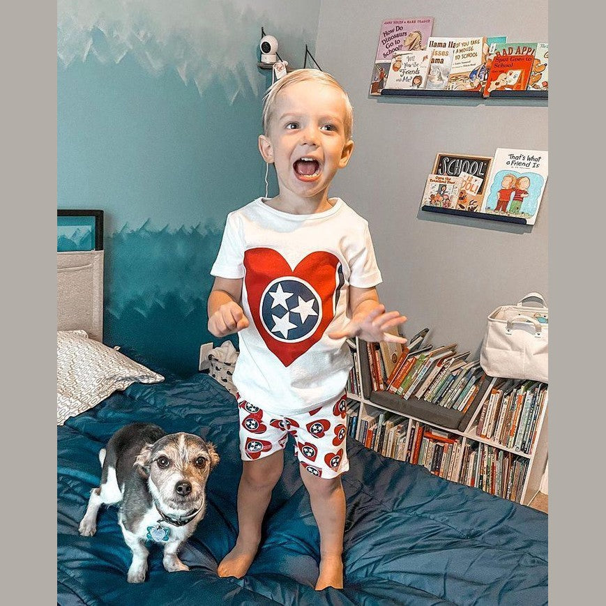 Toddler wearing Tennessee-themed pajamas with orange and white checkerboard pattern, smiling on a bed.