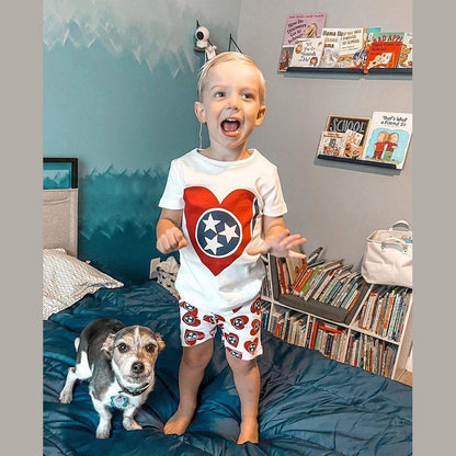 Toddler wearing Tennessee-themed pajamas with orange and white checkerboard pattern, smiling on a bed.