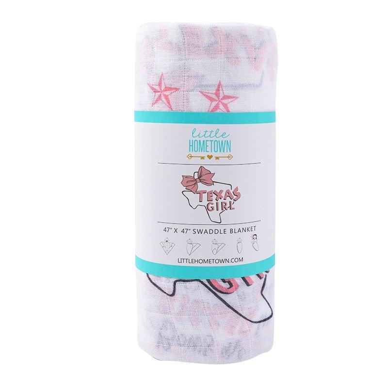 White muslin swaddle blanket with pink Texas-themed illustrations, including cacti, boots, and the word "Texas."