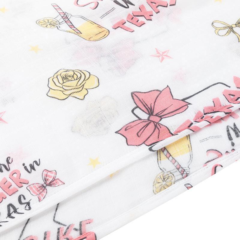 Texas-themed baby girl muslin swaddle blanket with pink accents, featuring state icons like boots and cacti.