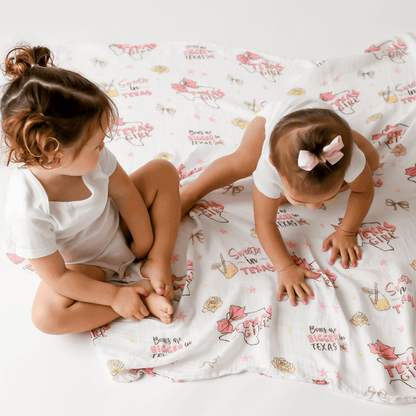Texas-themed baby girl muslin swaddle blanket with pink accents, featuring state icons and "Texas Baby Girl" text.