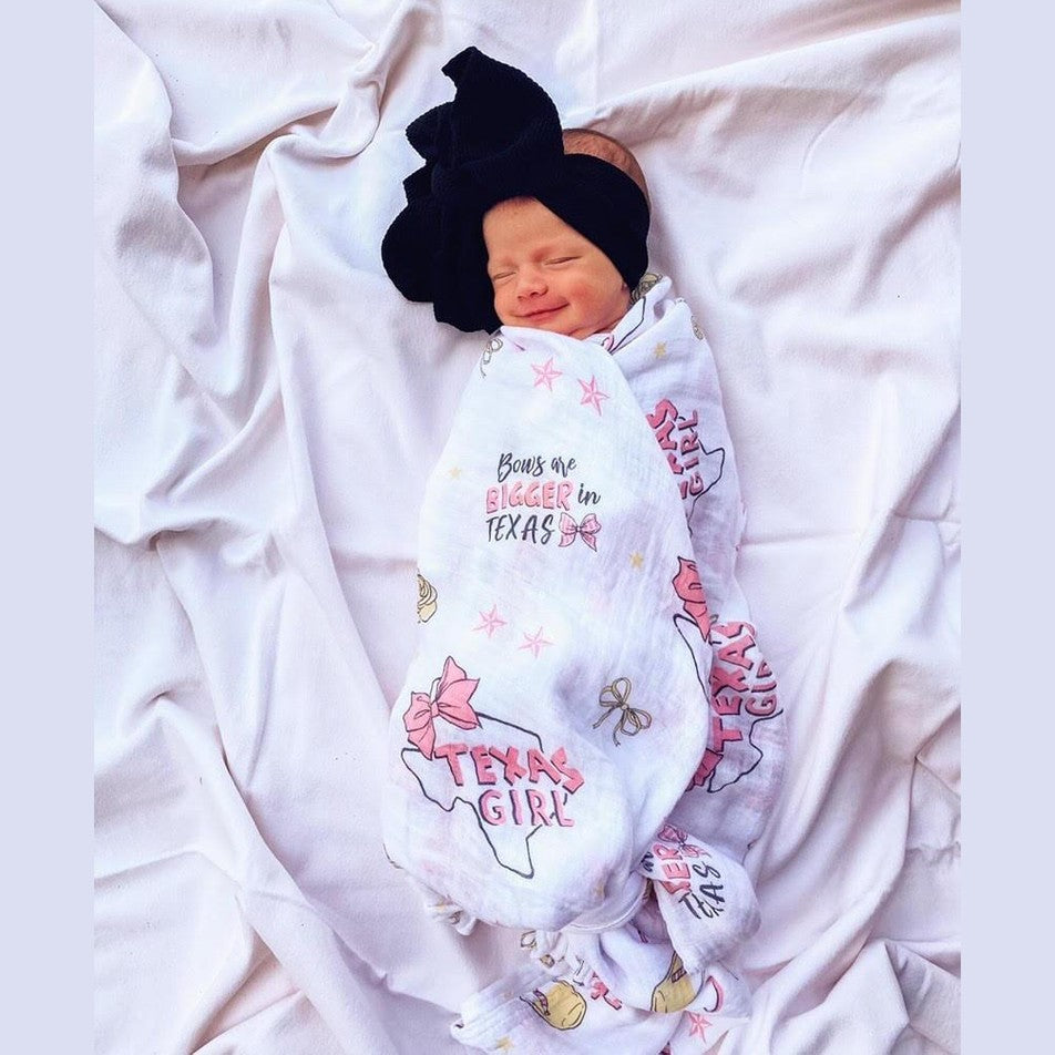 Pink muslin swaddle blanket with "Texas Baby Girl" text and state icons, including a cowboy hat and boots.