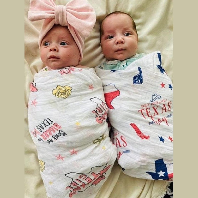 Texas-themed baby girl muslin swaddle blanket with pink accents, featuring state icons like cowboy boots and cacti.