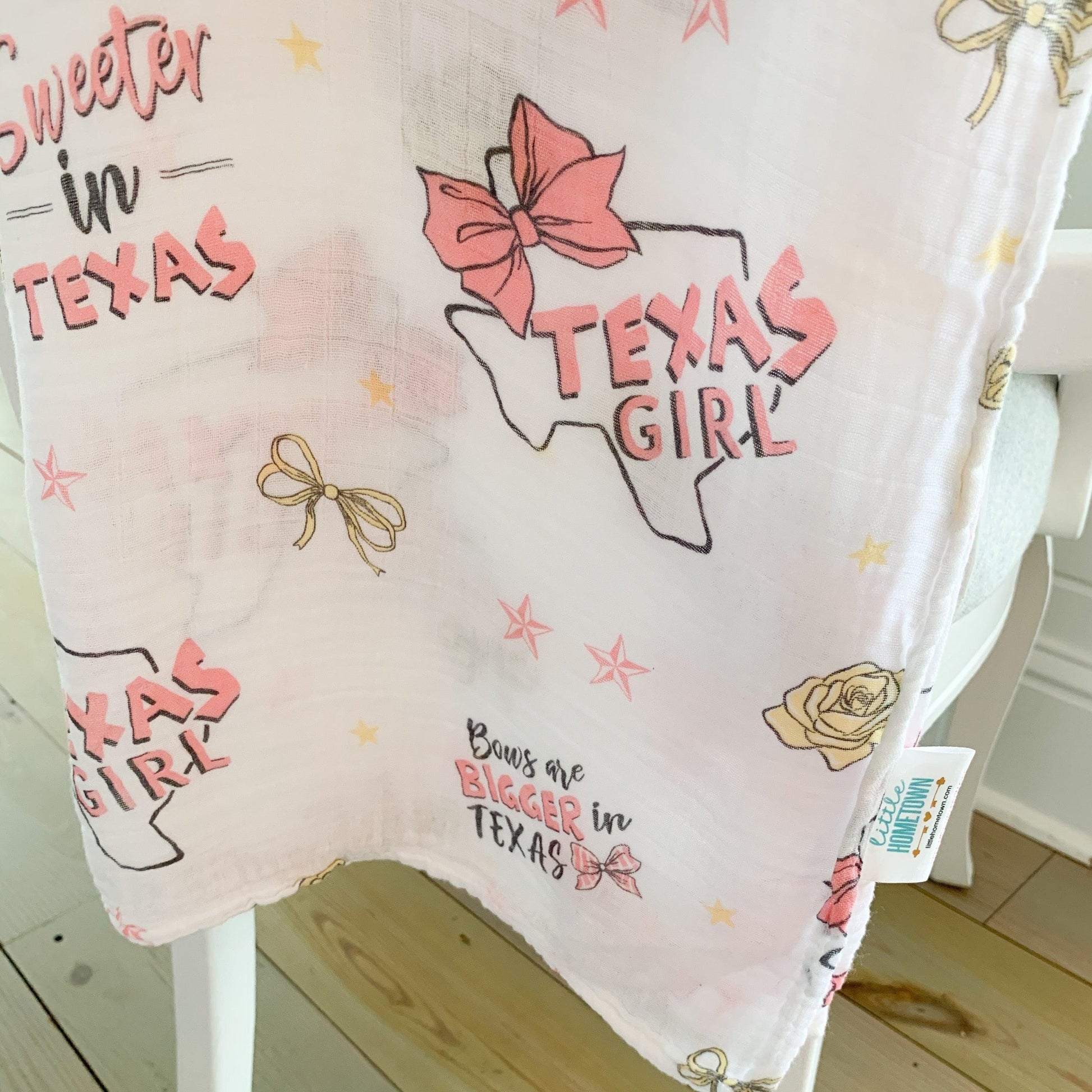 Texas-themed baby girl muslin swaddle blanket with pink accents, featuring state icons like boots and cacti.