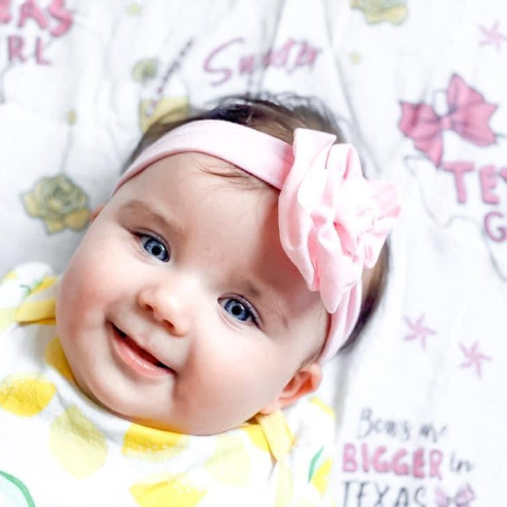 White muslin swaddle blanket with pink Texas-themed illustrations, including cacti, boots, and "Texas Baby Girl" text.