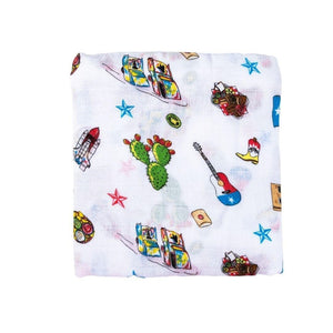 White muslin swaddle blanket with colorful Texas-themed illustrations, including cacti, cowboy boots, and armadillos.
