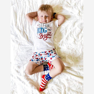 Child wearing Texas-themed pajamas with state icons, standing on a white background, smiling joyfully.