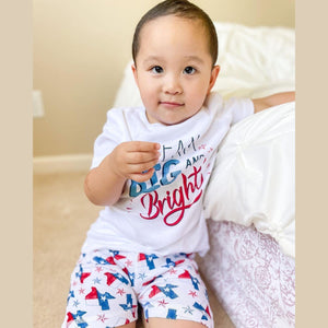 Child wearing Texas-themed pajamas with state icons, standing on a wooden floor, smiling joyfully.